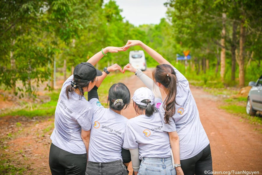 Employees wearing shirts with the slogan 'Giving Now' forming heart shape with their hands.